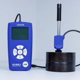 LS251D hardness tester displaying a measurement on its LCD screen, with the probe resting on a metal block.