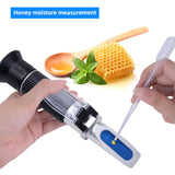 A hand holding a honey brix refractometer, with a blurred background of a bee hive.